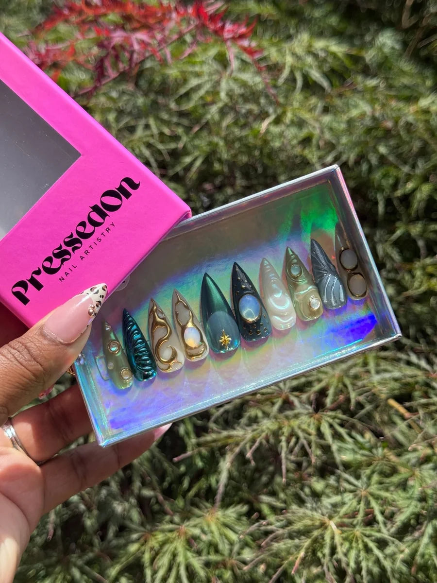 Medium press-on nails with ethereal moonstone and celestial charmed designs. They feature green, gold, white, and navy colors, along with gemstone and star embellishments.