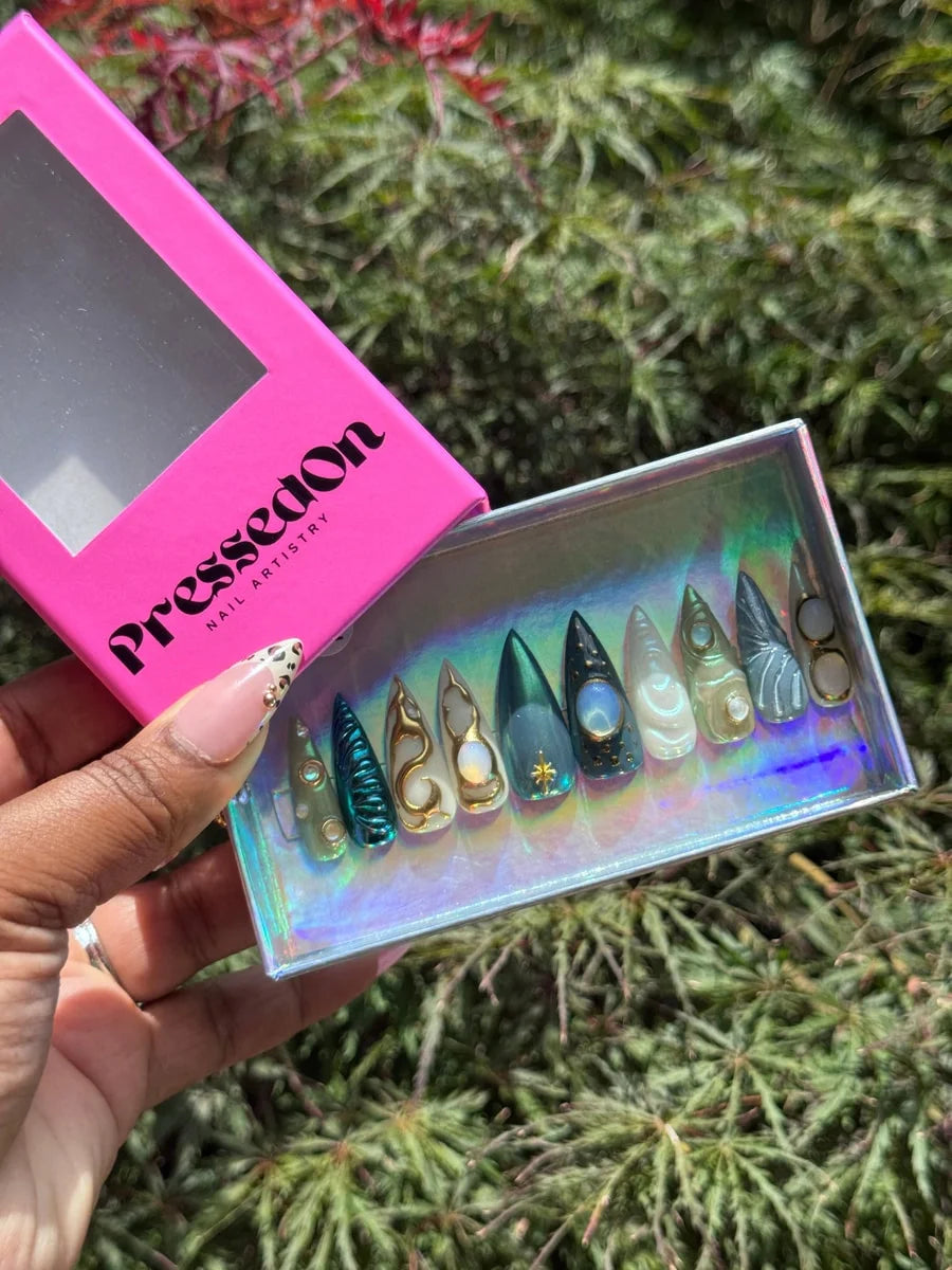 Medium press-on nails with ethereal, moonstone, and celestial-themed art. They feature various colors including green, gold, and white with star, gemstone, and orb embellishments.