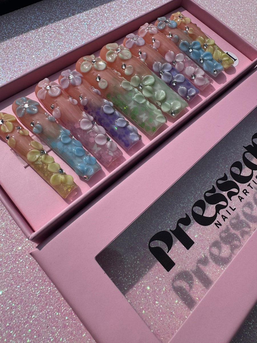 Multi-colored, extra long press-on nails with a floral design. Each nail has 3D flower charms and small rhinestone accents.