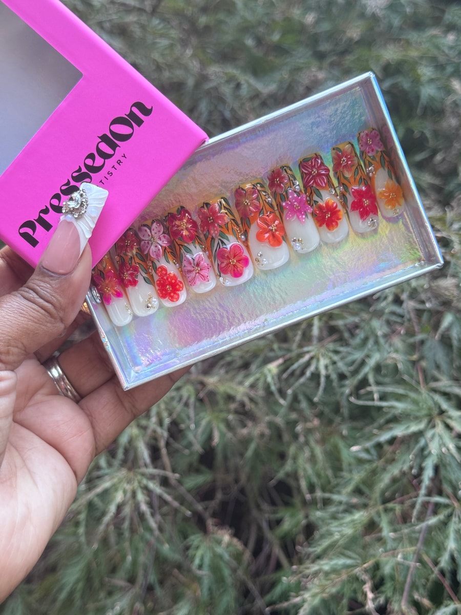 Medium-length press-on nails with a floral garden design featuring painted flowers in pink, red, orange and yellow, and rhinestone accents.