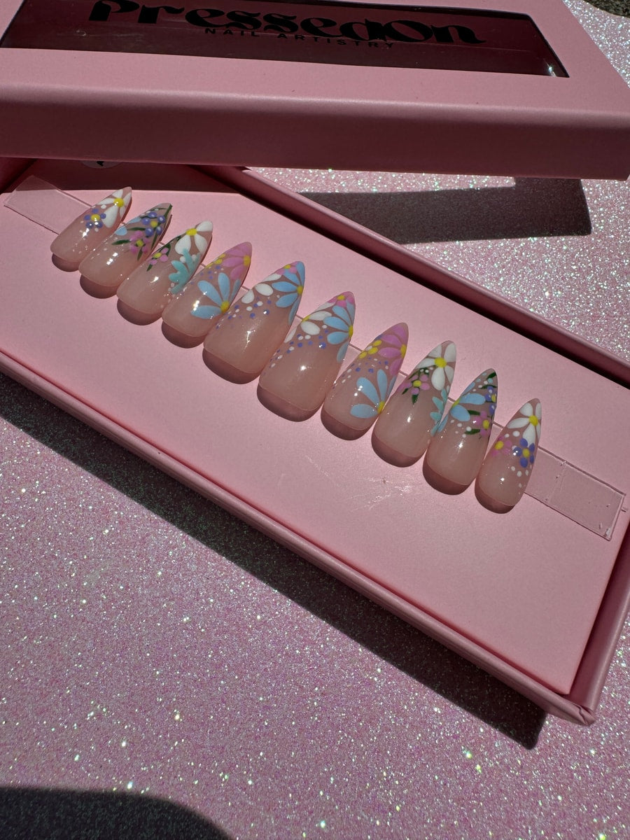 Set of stiletto-shaped press-on nails with a short length and glossy finish. The nails have a floral garden design featuring pink, blue, and white flowers.