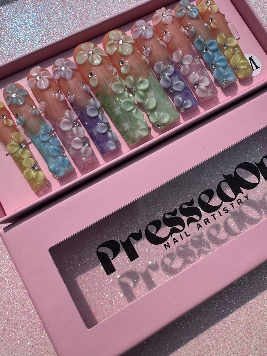 Pastel-colored extra long press-on nails with 3D flower decorations and sparkly crystal accents.