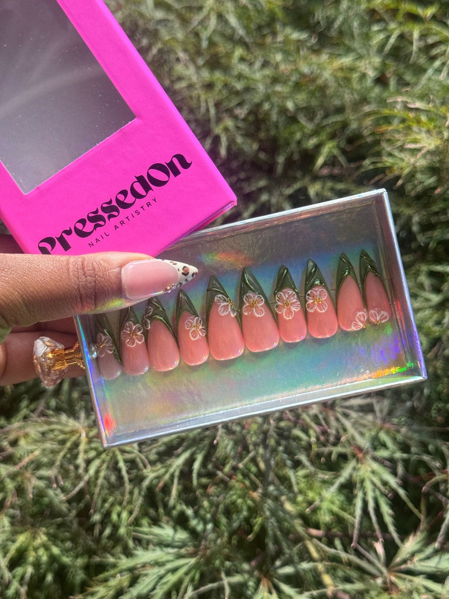 Pink medium press-on nails with green tips and delicate white jasmine flower designs with gold accents. The nails have a glossy finish.