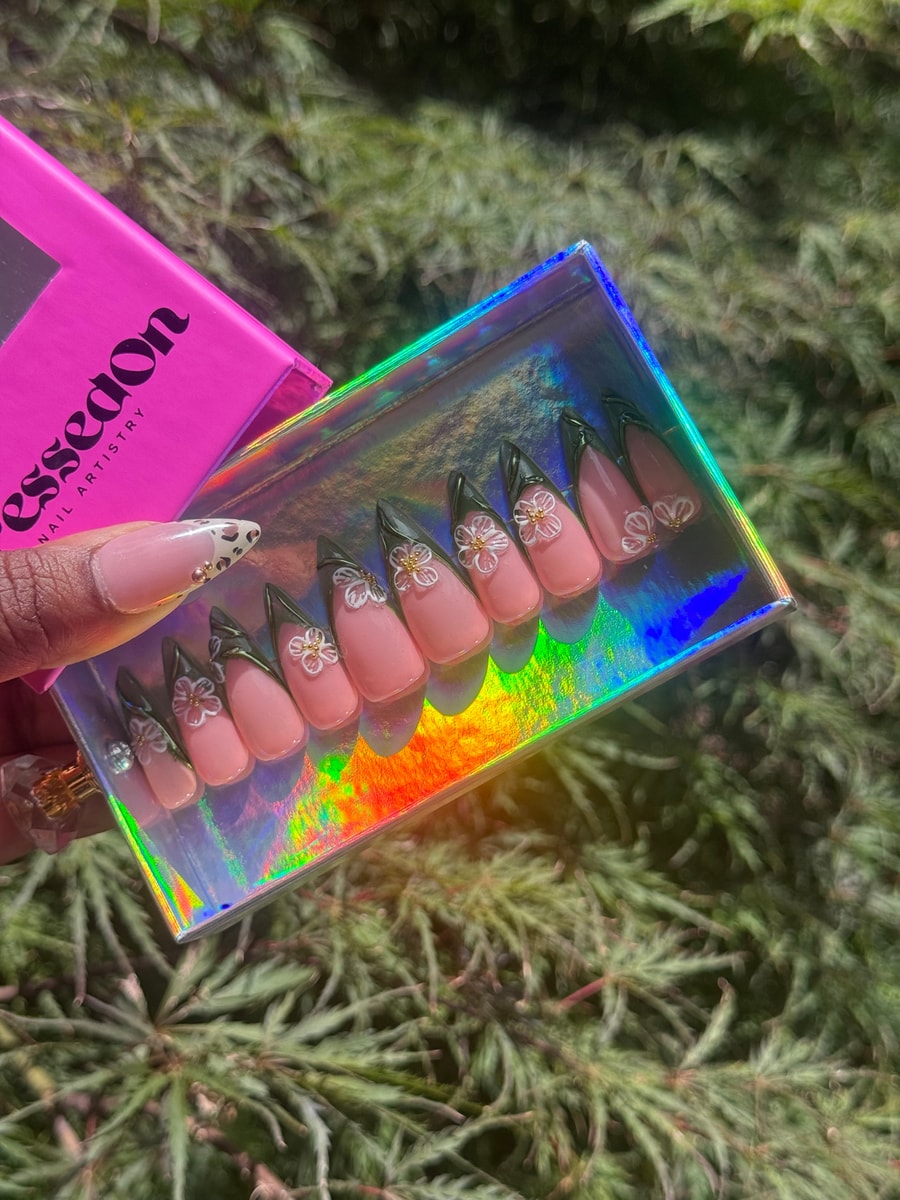 Medium length pink press-on nails feature dark green French tips and a delicate white jasmine flower design on each nail.