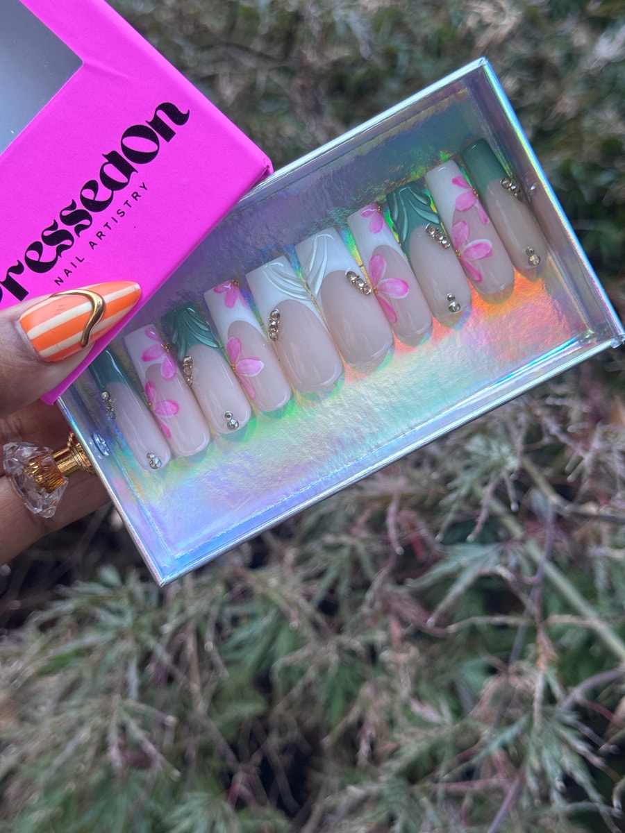 Medium press-on nails with a floral paradise design. They feature pink flower accents, green leaf details, gemstone embellishments, and French tip variations in white and green.