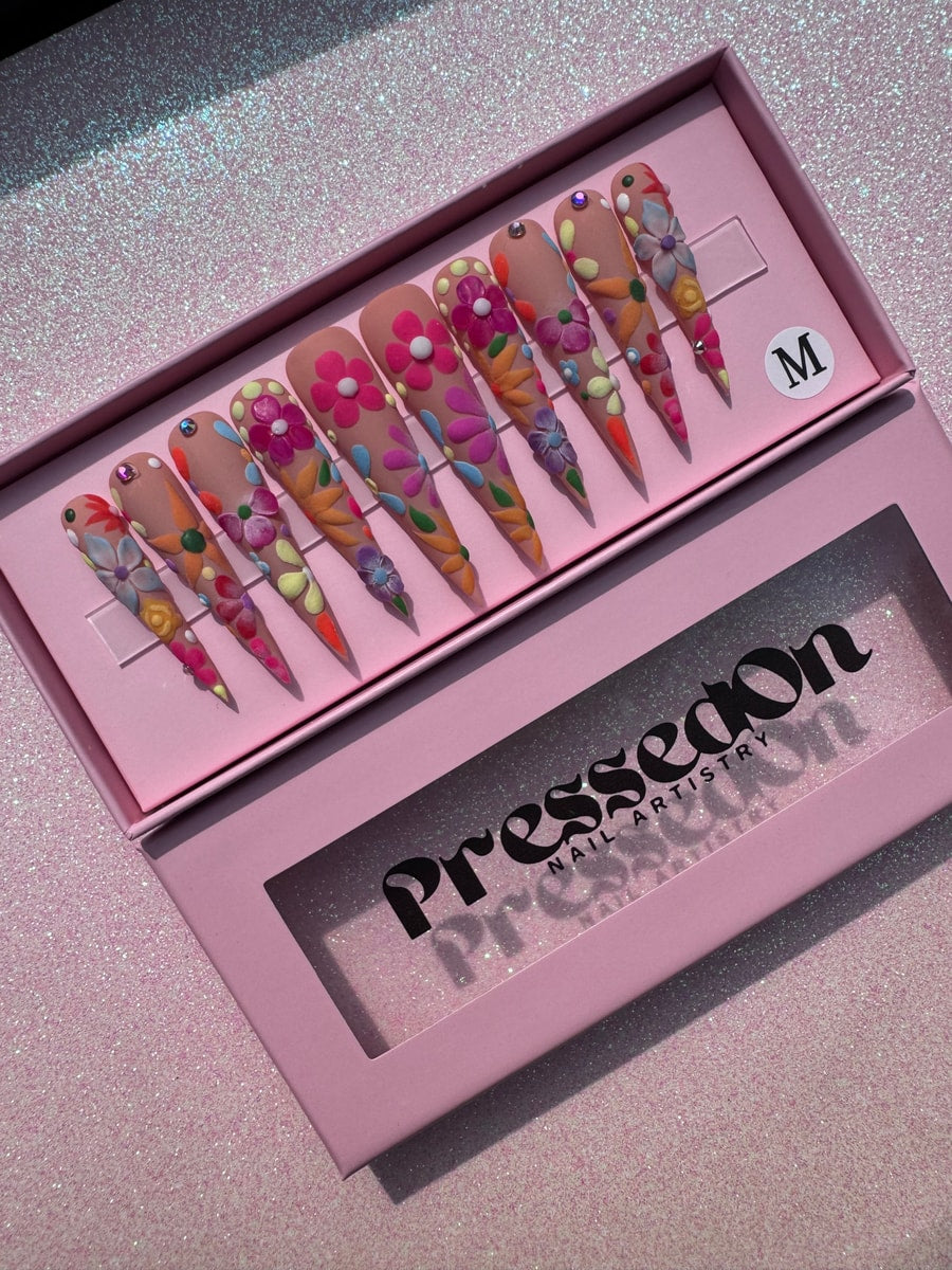 Xtra long stiletto press-on nails with light skin tone base and 3D floral art in pink, orange, purple, yellow, and green.