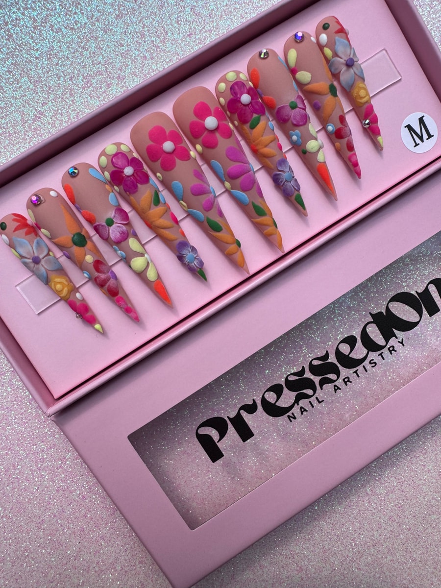 Set of extra long stiletto press-on nails with nude base and colorful floral designs. Iridescent gems add sparkle.
