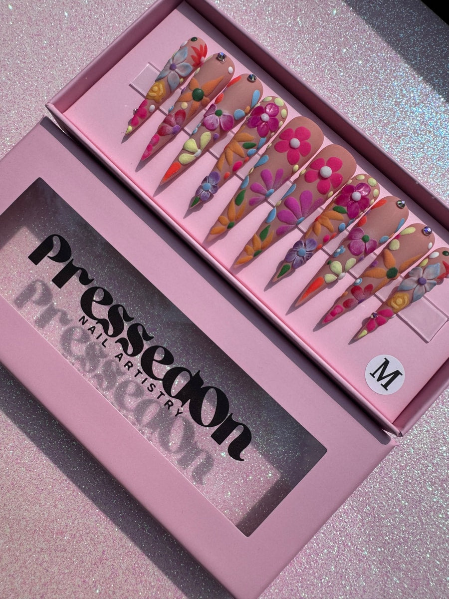 Xtra long stiletto press-on nails with colorful 3D flower decorations. Each nail has unique floral art in pastel colors.