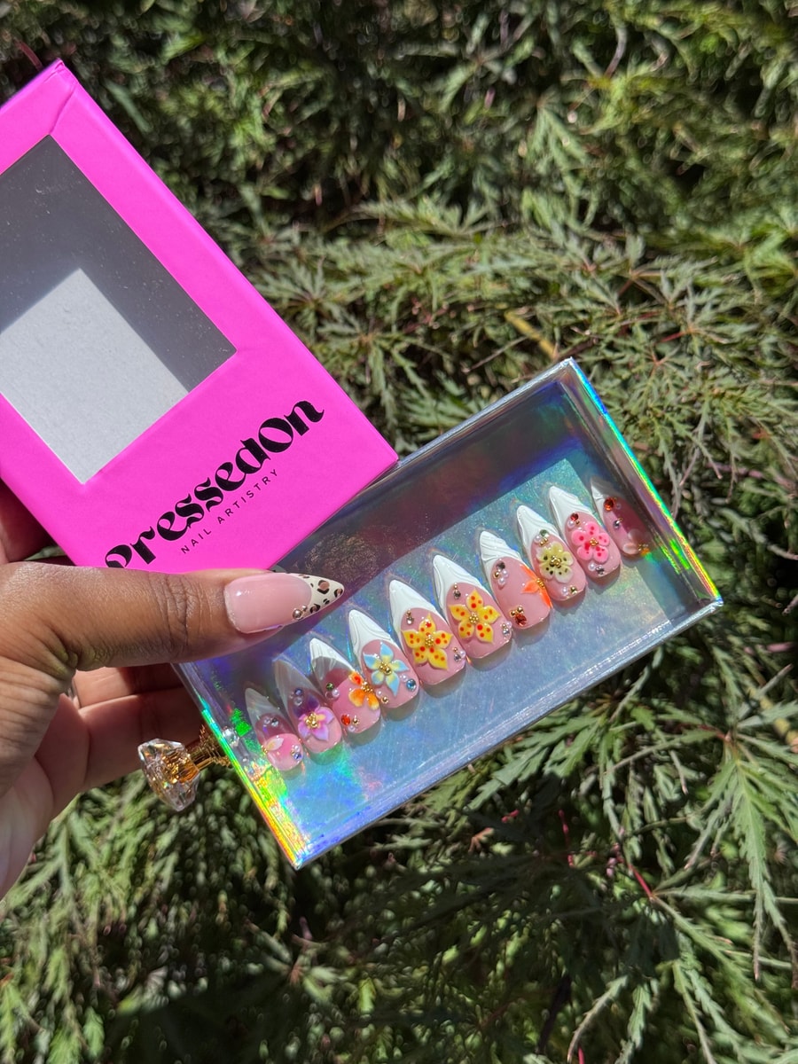 These are short press-on nails with a pink base, white French tips and 3D flower accents. The nails feature colorful floral designs and pearl embellishments.