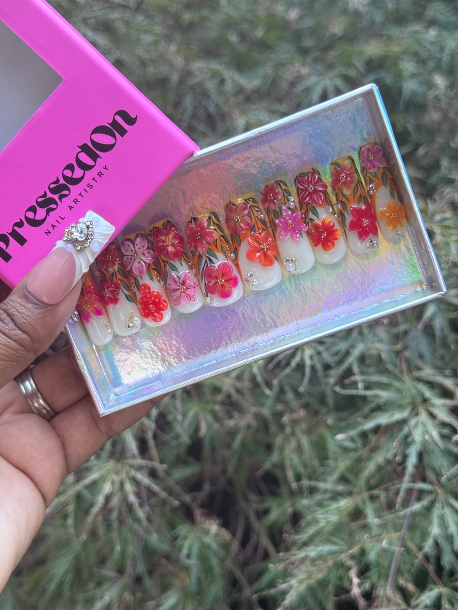 Medium length press-on nails with a white base and painted floral designs in pink, red, and orange. They are decorated with pearls and small gemstones.
