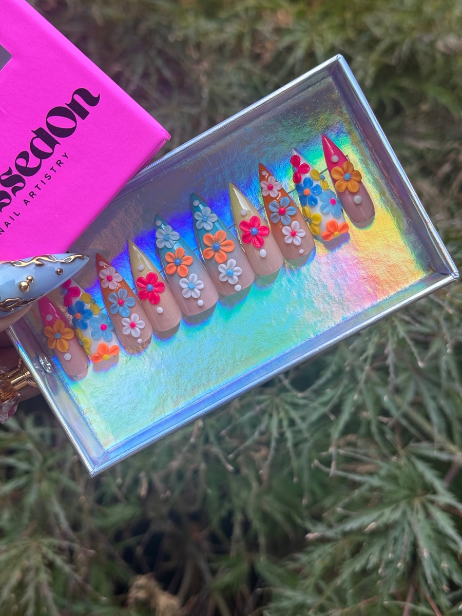Short press-on nails decorated with colorful flower designs and white dots for a floral effect.