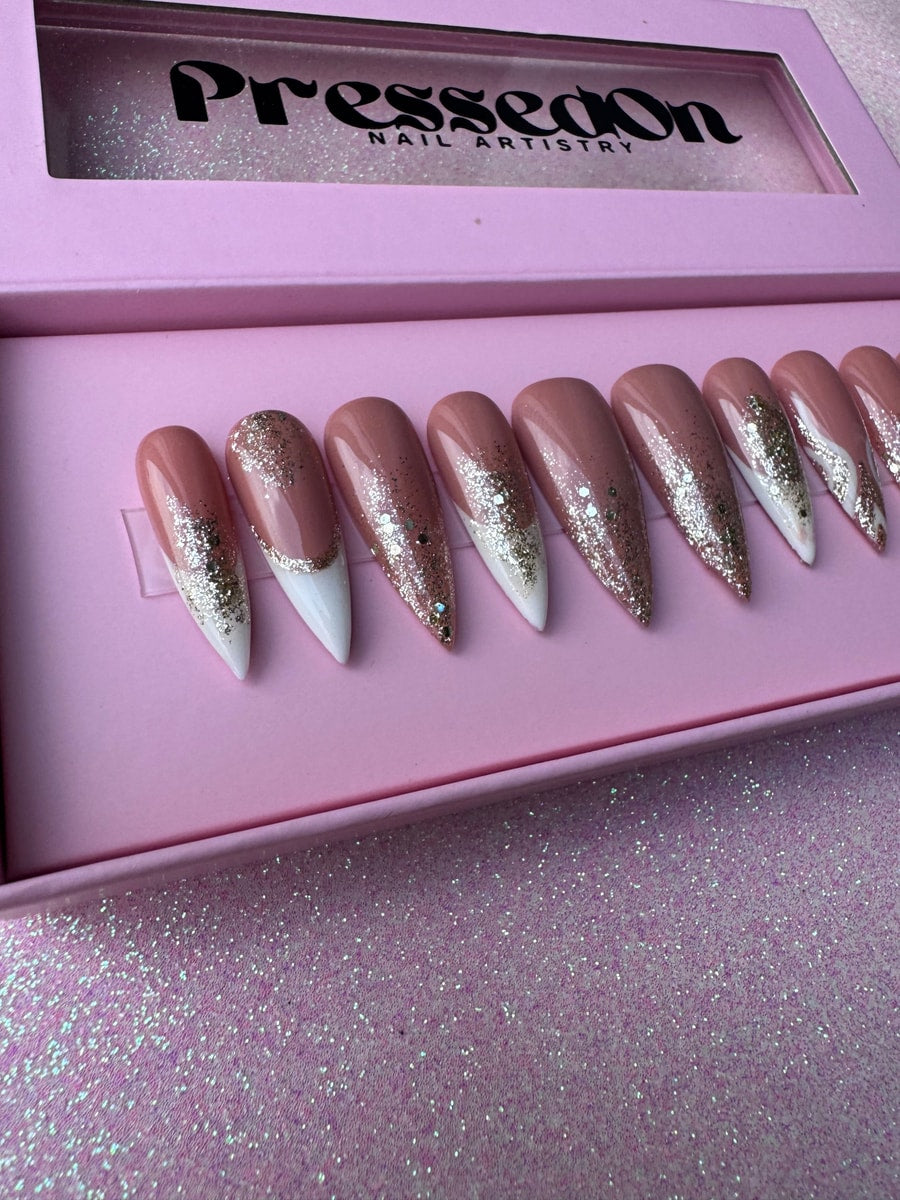 Medium length press-on nails feature nude polish, white French tips, and sparkling silver glitter detailing.