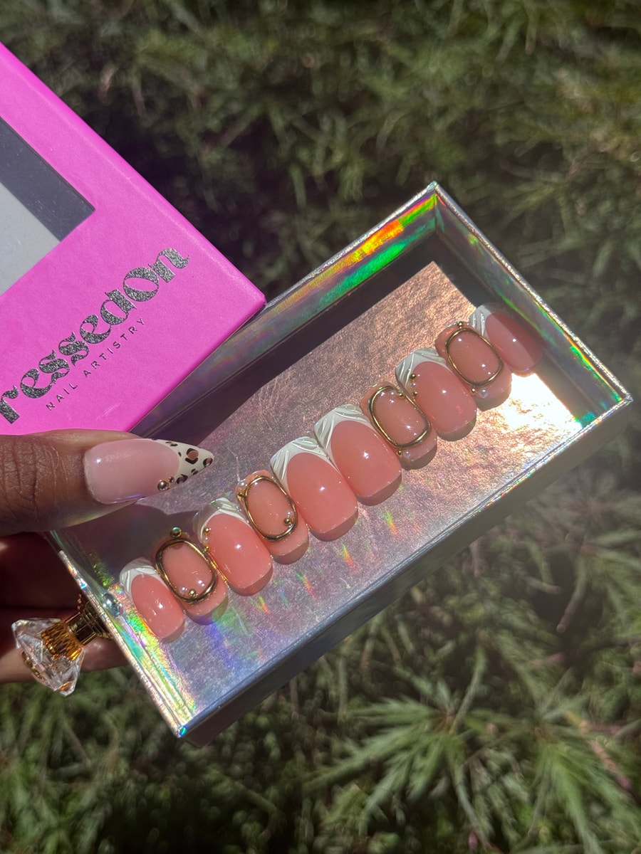 Set of short press-on nails with a French tip design and gold oval accents. One nail has a cheetah print pattern.