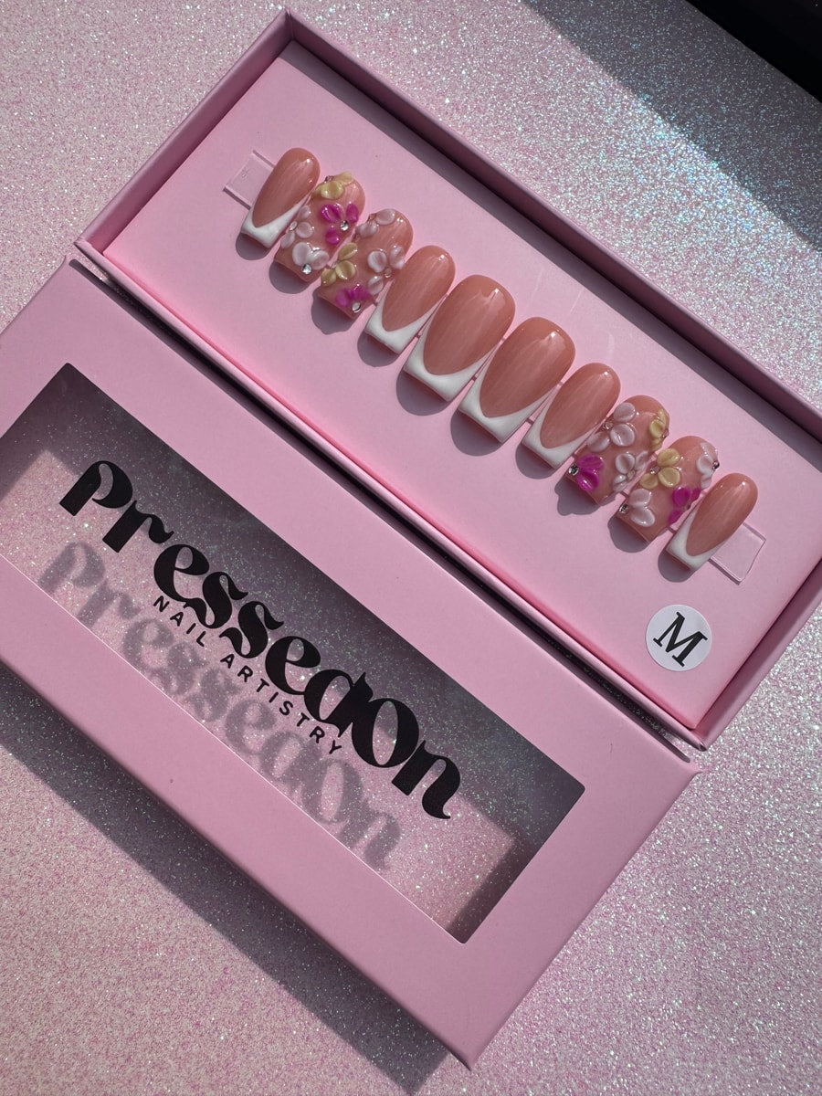 Set of short, nude press-on nails featuring white French tips and 3D floral designs with pink and yellow flowers and rhinestone details.