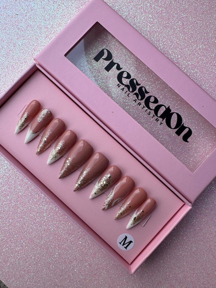 Nude and gold glitter press-on nails in medium length. Some nails have white French tips, while others are decorated with gold glitter.