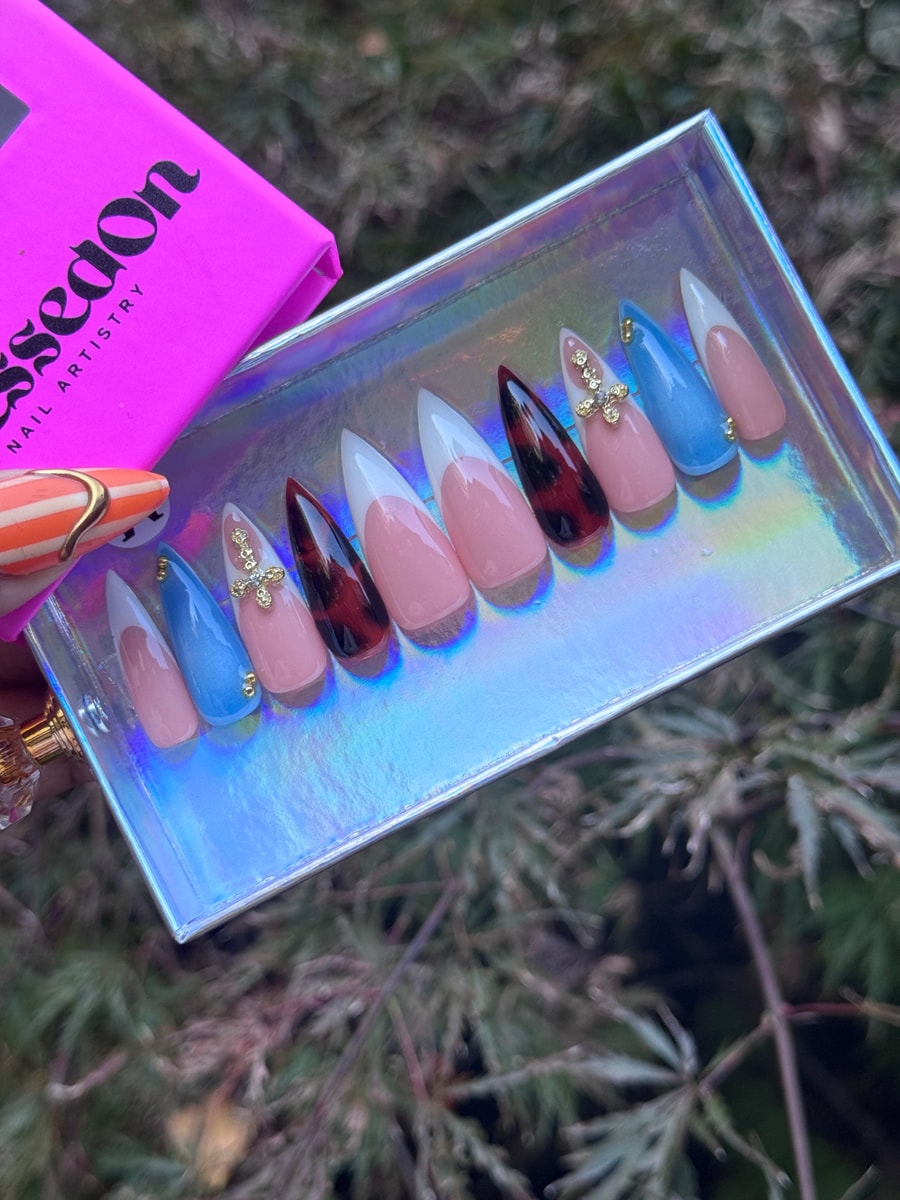 Medium-length stiletto press-on nails featuring a French twist design. Includes classic pink French tips, blue nails, tortoise shell nails, and gold cross charms.