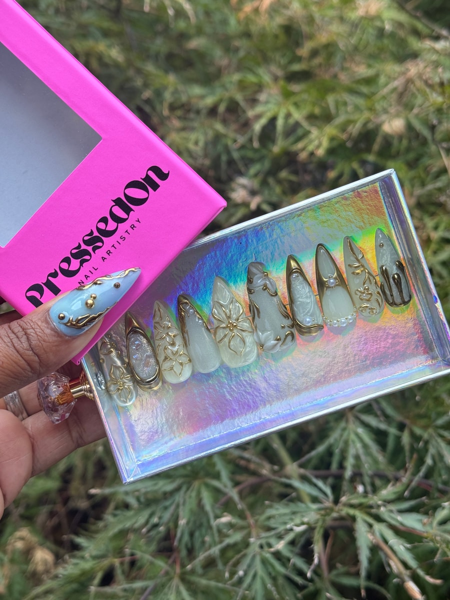 Frosty white short press-on nails with intricate gold floral designs and pearl accents.  Several nails have a dripping gold effect for added detail.