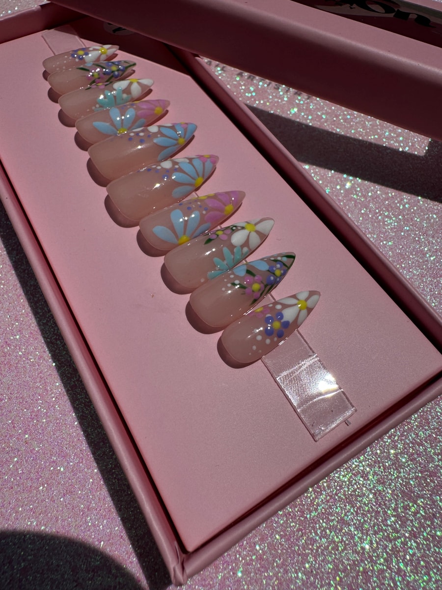 Short, almond-shaped press-on nails with a clear base and pastel floral designs. The nails feature daisies in blue, pink, and white, with a smattering of small polka dots.