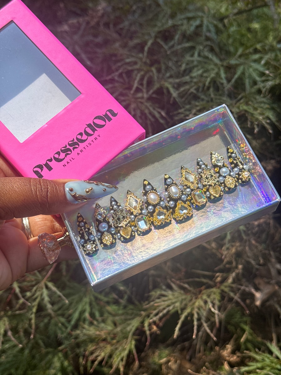 Short black press-on nails feature an array of shimmering gems, pearls, and gold accents for a luxurious and ornate design.