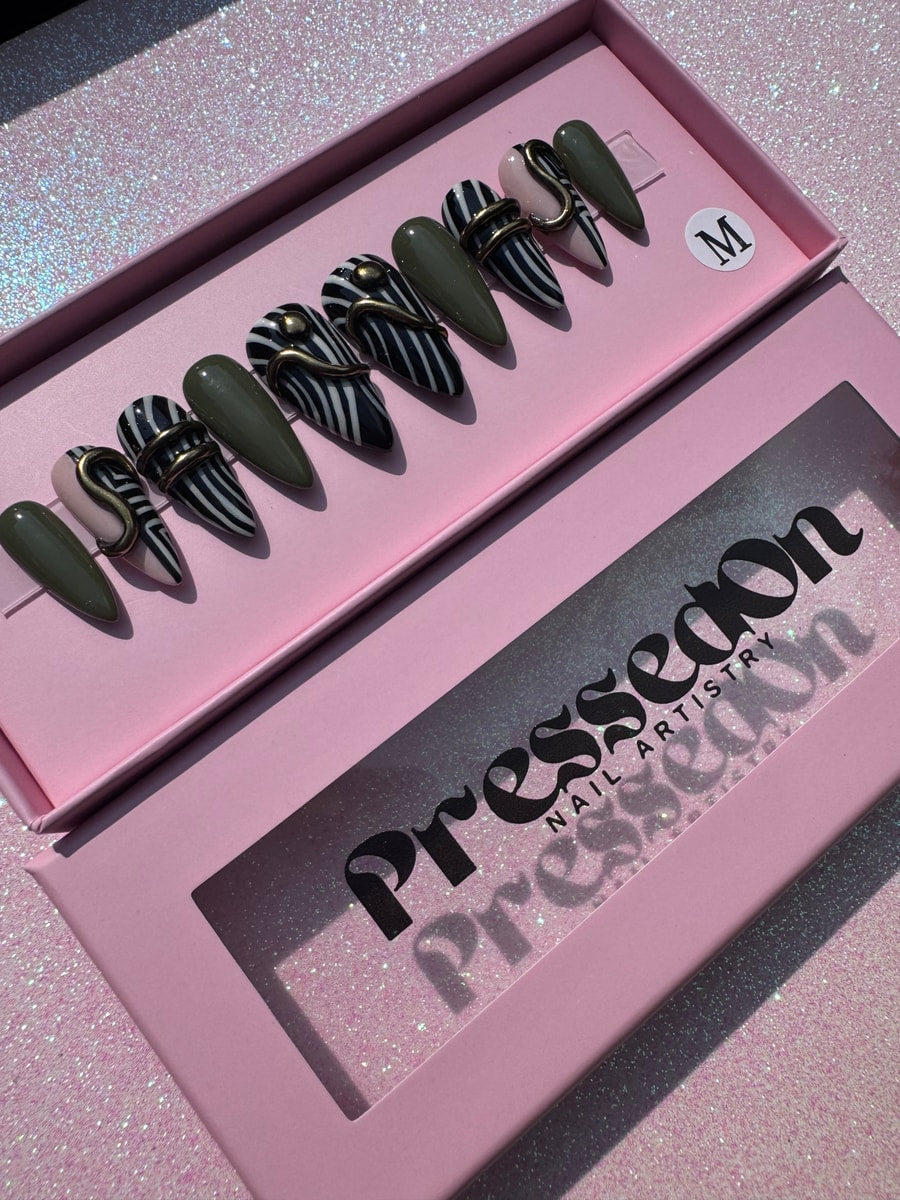 Set of stiletto press-on nails with an olive green, zebra striped, and geometric design. Some have gold coiled accents. One is light pink.