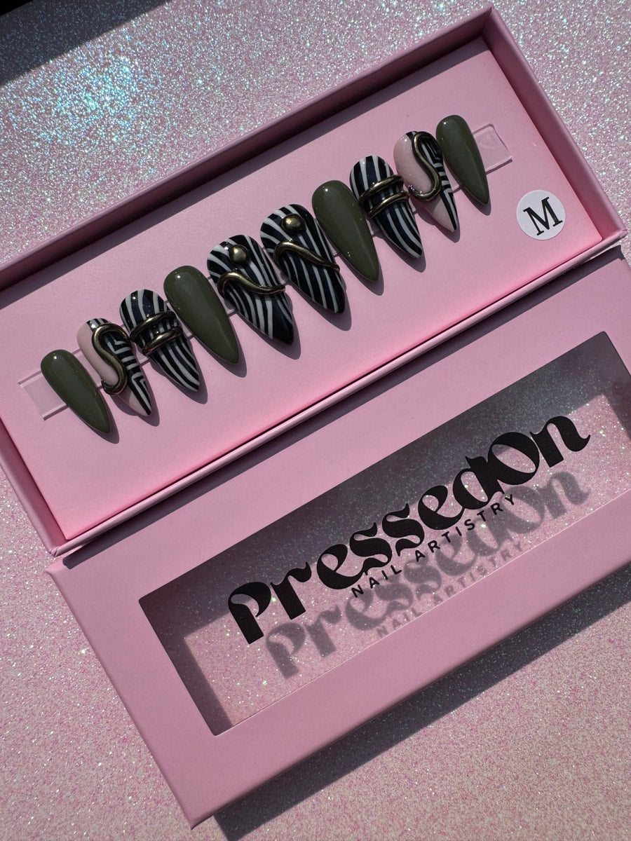 These short press-on nails feature an olive green color and a black and white zebra stripe pattern, accented with gold embellishments.