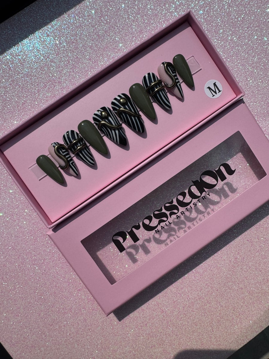 Set of short stiletto press-on nails features zebra stripes, olive green, nude, and gold hardware. 