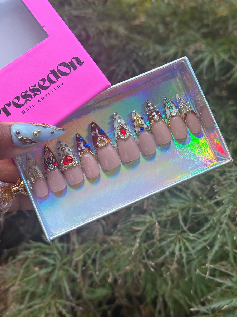 Short, glam press-on nails featuring a French tip design and rhinestone embellishments. Each nail includes decorative charms, beads, and gems.