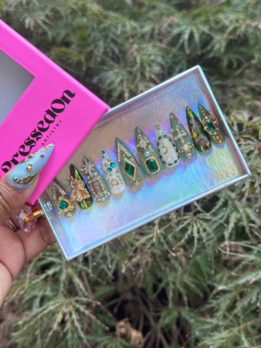 These short press-on nails feature goddess designs with emeralds, gold accents, stars, moons, and portraits on a white and light green base.