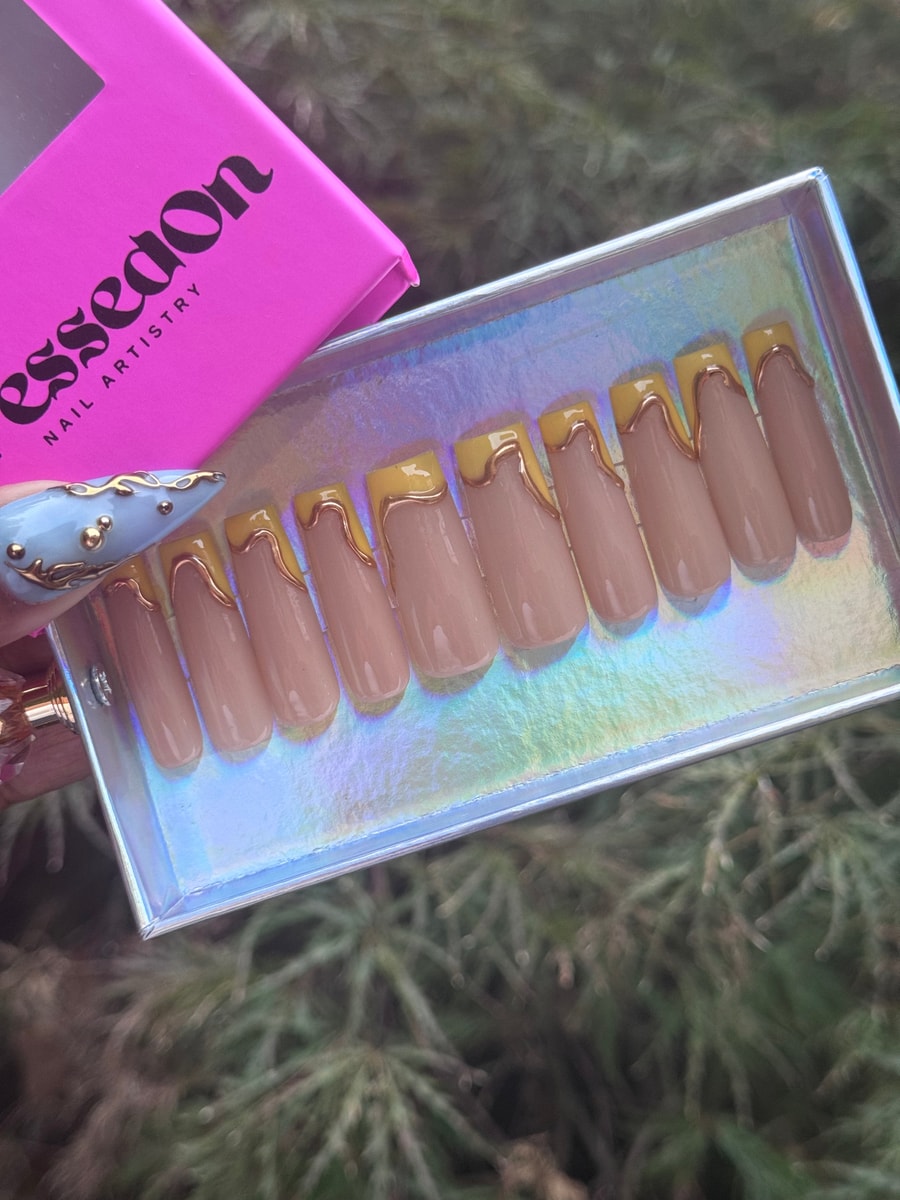 Medium-length nude press-on nails with dripping gold accent and yellow French tips.