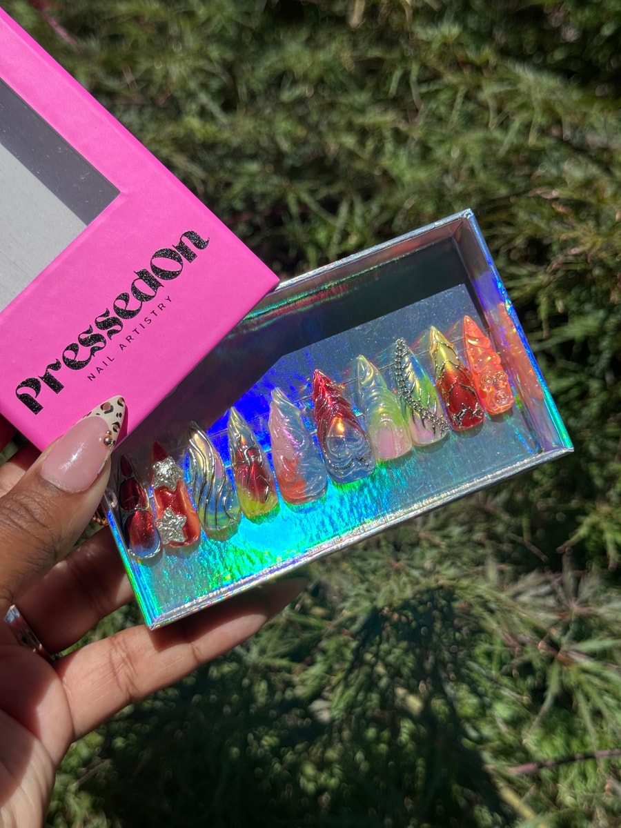 Medium-length press-on nails with assorted designs, colors, and holographic accents. Designs include abstract art and gemstone embellishments.