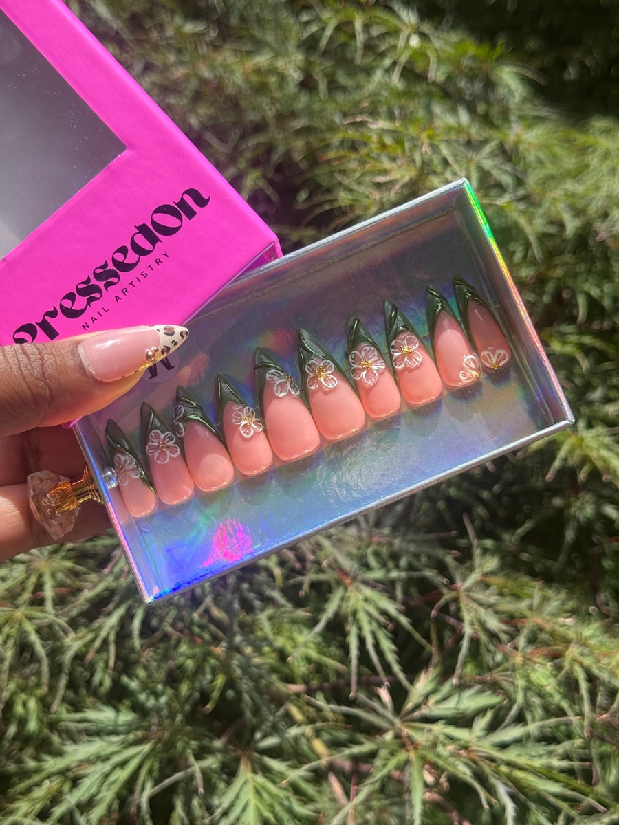 Peach-colored medium press-on nails with dark green tips. Each nail has a delicate 3D white jasmine flower with a gold center.