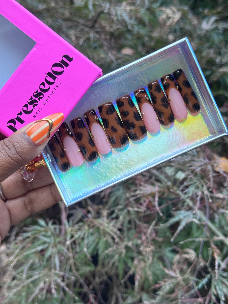 Medium-length press-on nails with a brown and black leopard print, pink base, and gold stud accents.