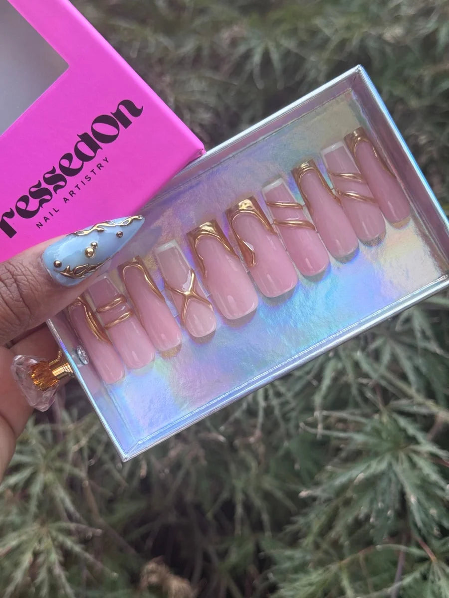 Set of medium pink press-on nails with glossy finish. They feature gold line art with curved and criss-cross designs.