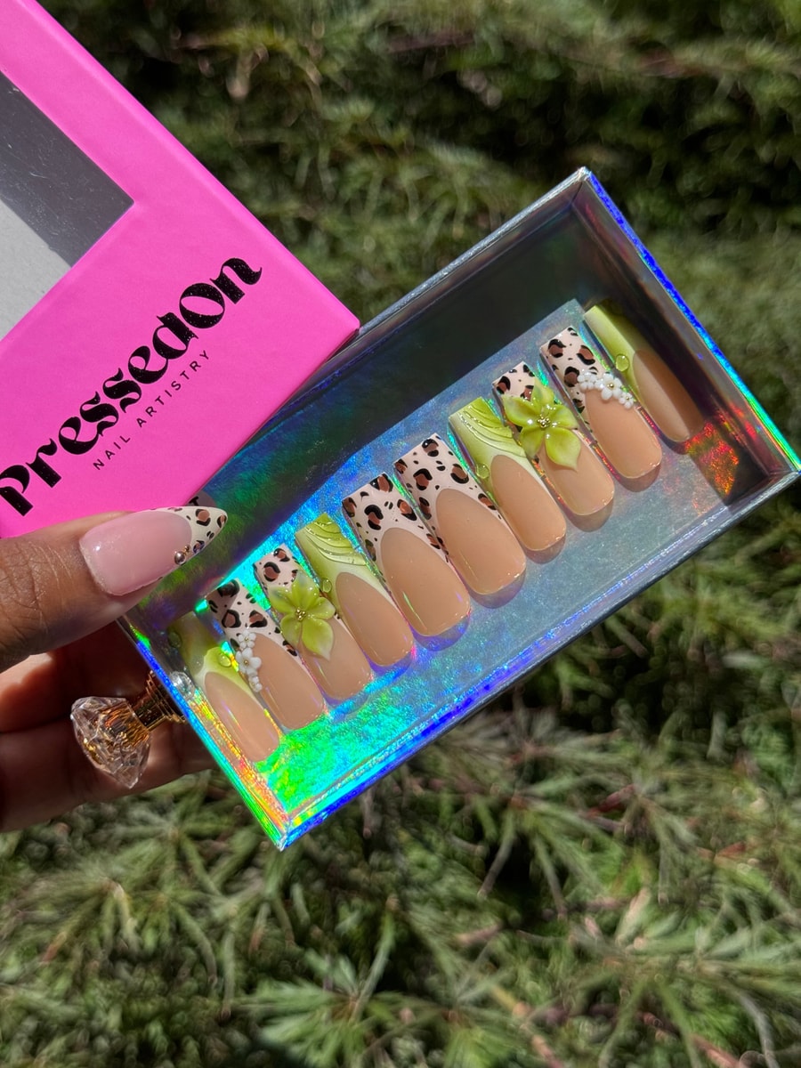 Medium length press-on nails with a cheetah print, lime green French tips, peach base, and flower embellishments on some nails.