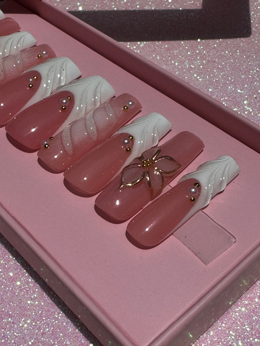 Clear pink long press-on nails with white accents. Several nails have pearl beads and one has a gold flower. 