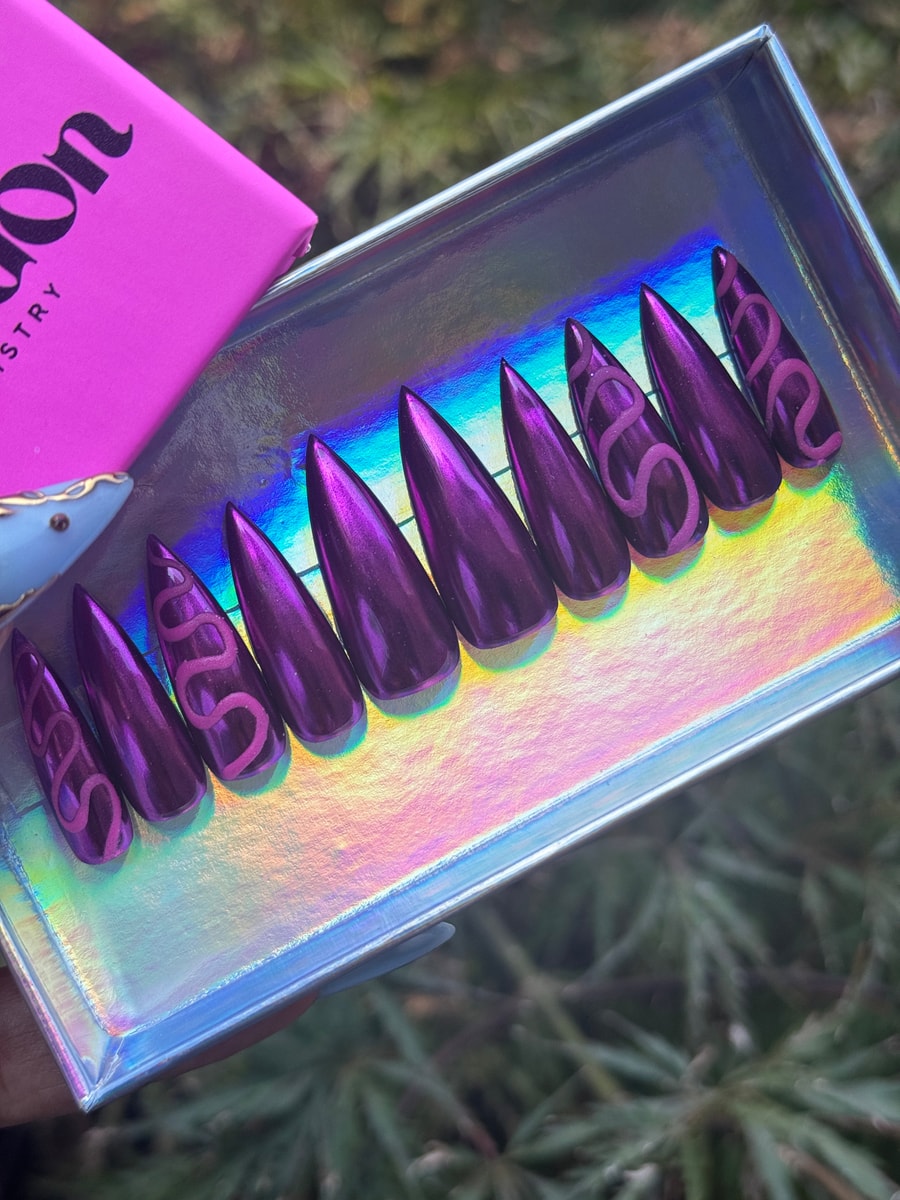 Set of magenta stiletto-shaped press-on nails with a metallic finish. Some nails feature a pink snake design.