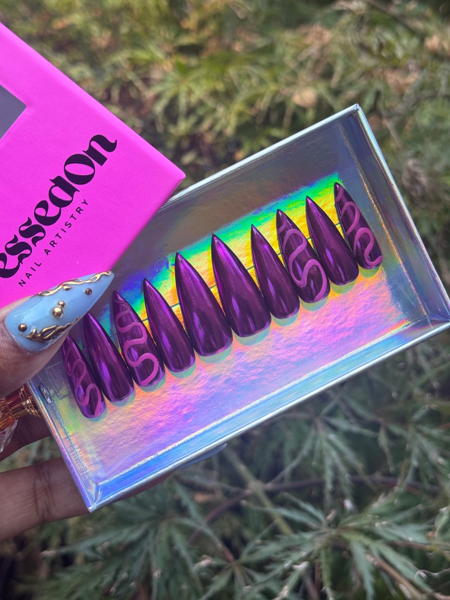 Magenta stiletto press-on nails are displayed with a light pink snake design on each nail.