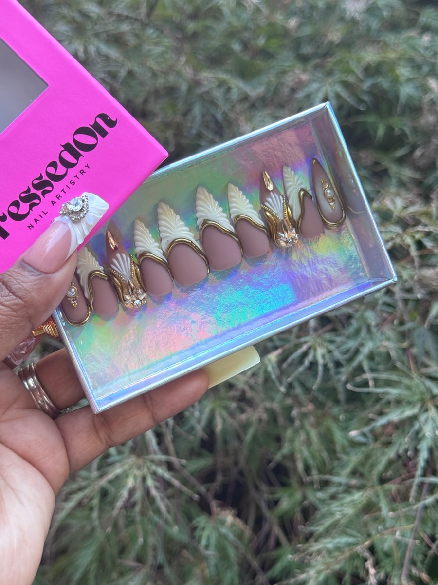 Brown medium press-on nails with gold and white 3D designs, and small rhinestone embellishments.