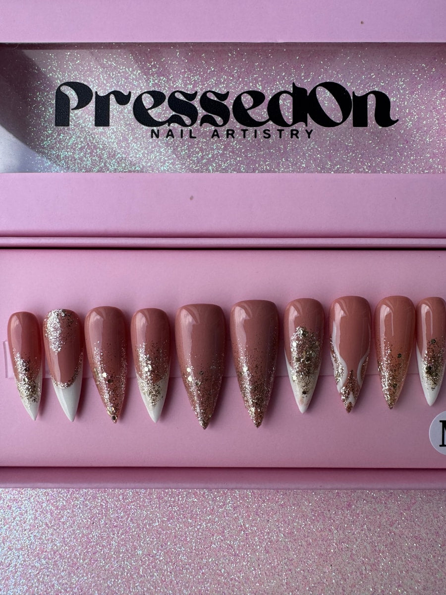 Set of stiletto shaped press-on nails. They feature a pink base, white French tips, and gold glitter accents on some nails.