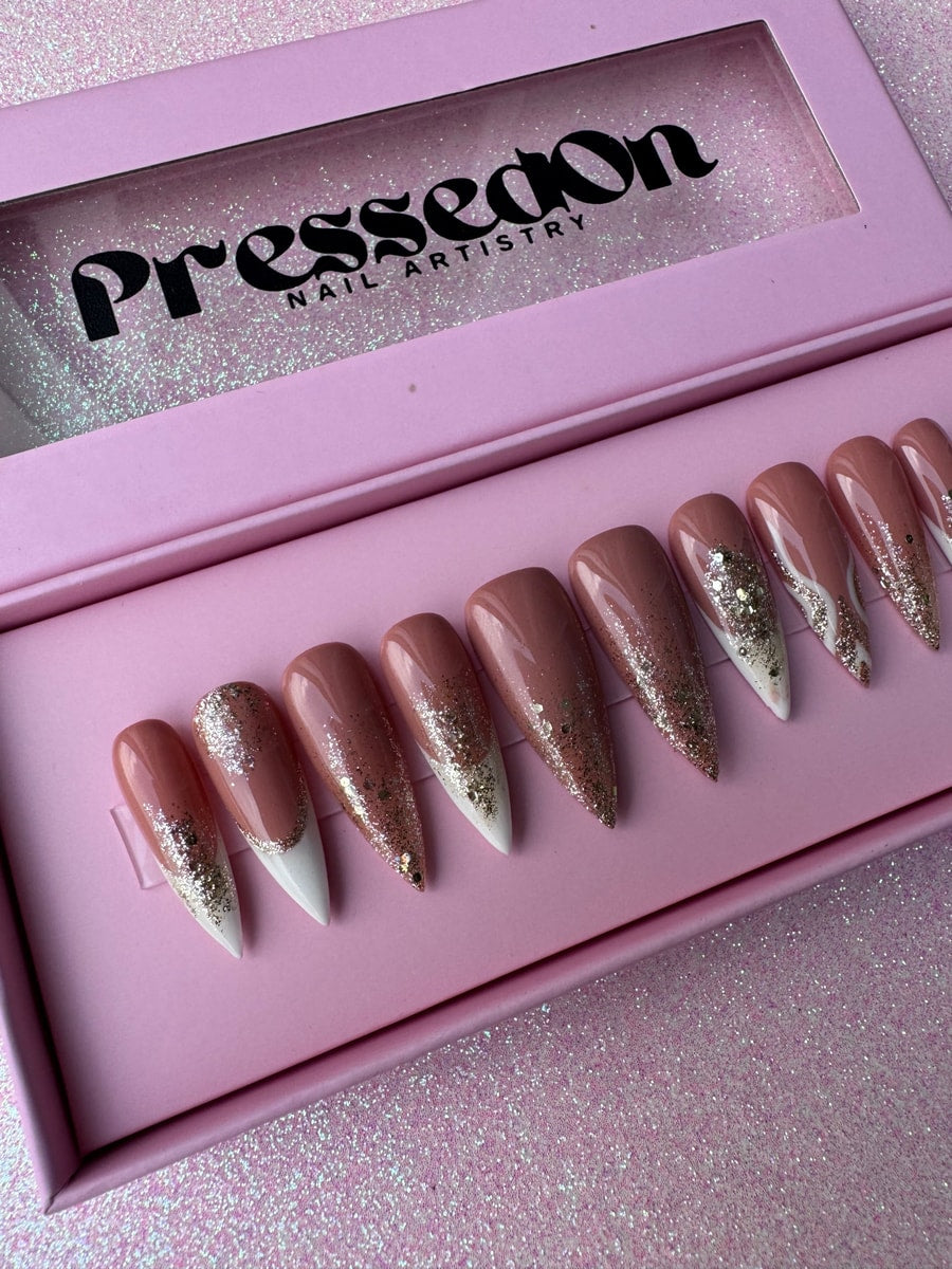 Nude and white French tip press-on nails with gold glitter accents, some having a heavier glitter concentration at the tips.