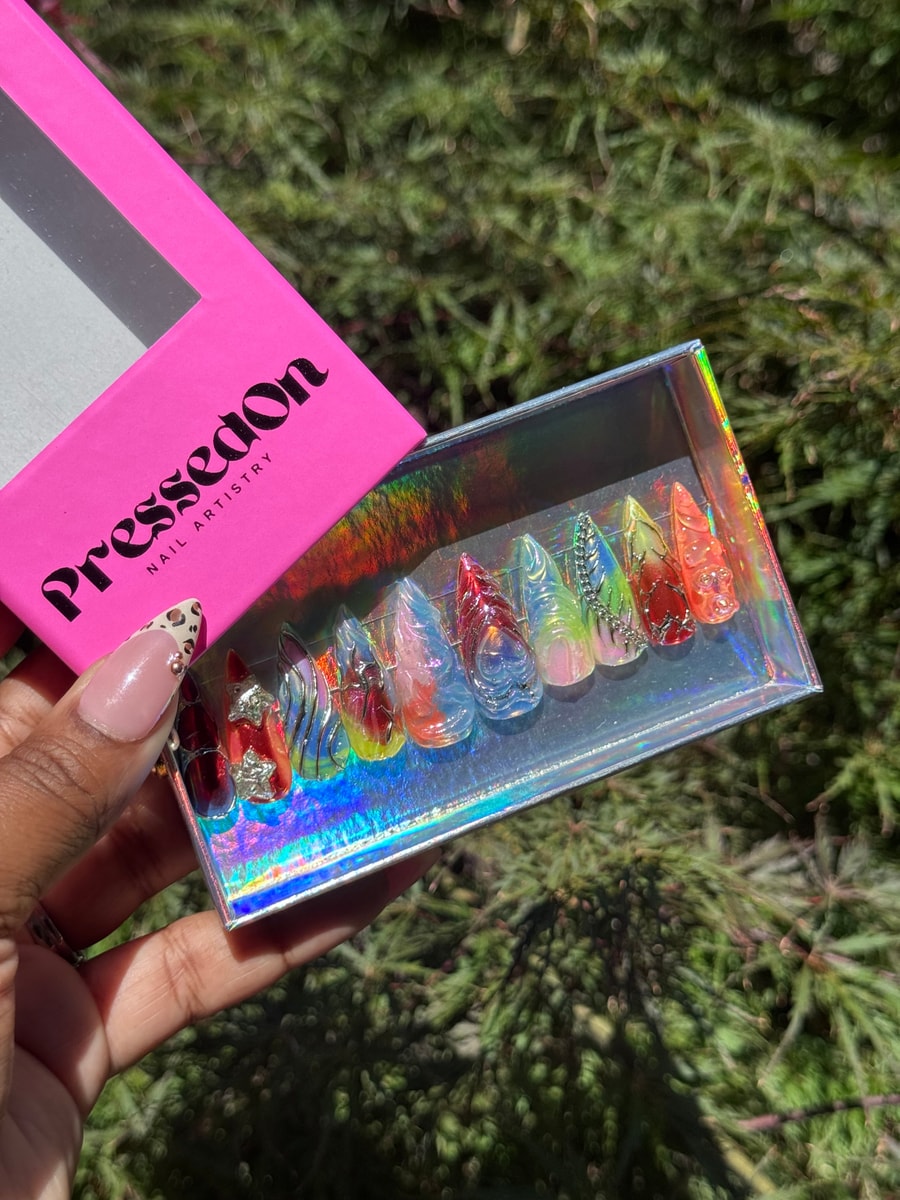 A set of medium-length press-on nails with a clear, iced, jelly-like finish. Nails are decorated with red, yellow, and blue colorways and 3D metallic accents.