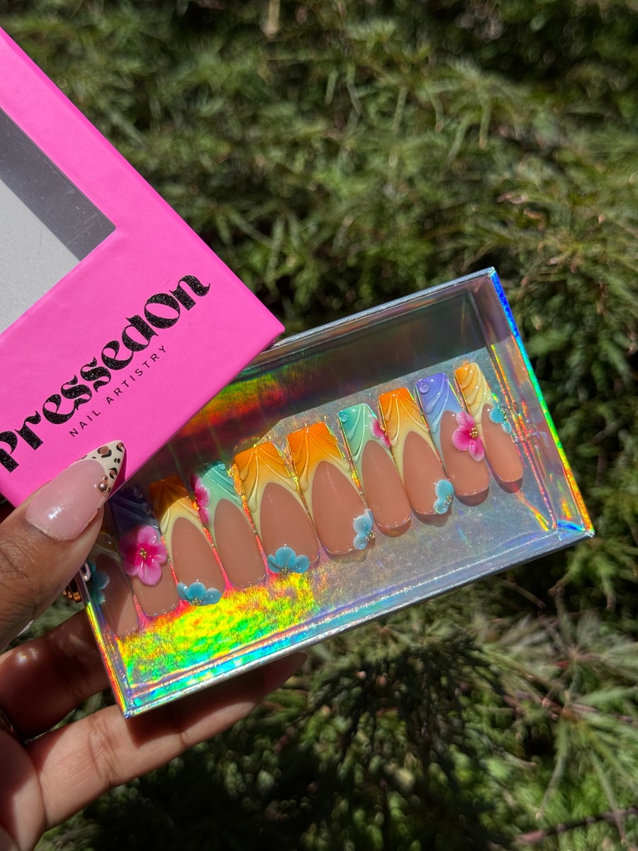 Set of medium-length press-on nails with rainbow gradient tips, white French and 3D flower decorations. The flowers accent the overall design.