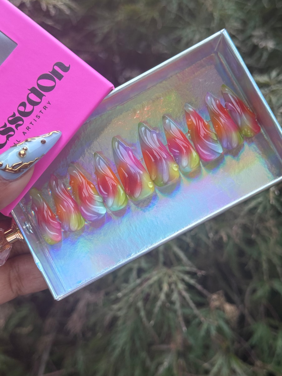 These are medium length stiletto press-on nails with an abstract rainbow swirl design. The nails are mostly translucent.