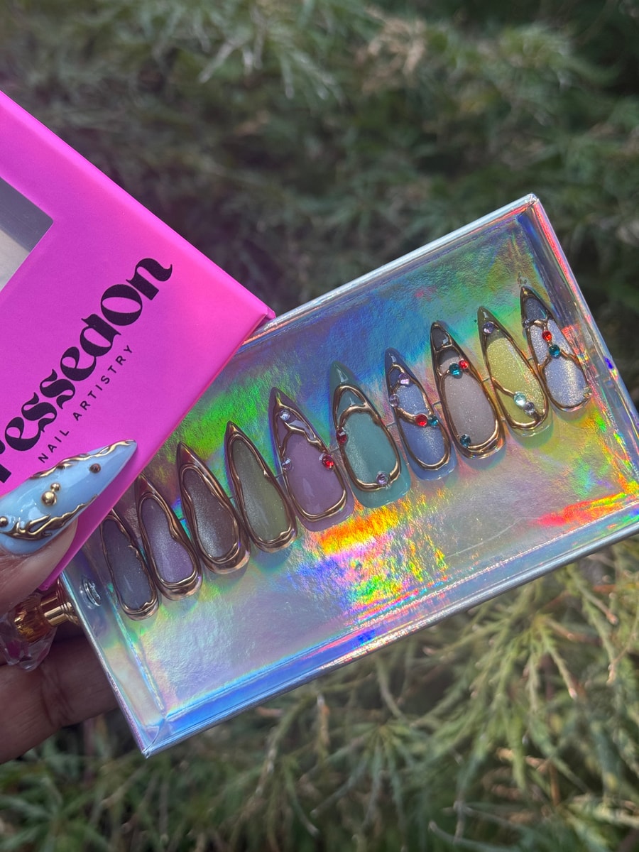 Collection of short stiletto press-on nails with gold accents and multi-colored gems. The nails have a unique design, featuring gold outlines and a variety of pastel shades.