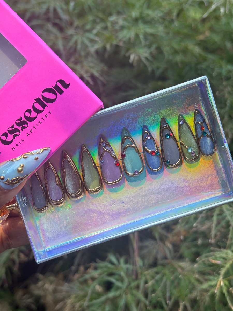 These short press-on nails feature a golden frame design with gemstone accents. Colors include shades of purple, blue, and green.