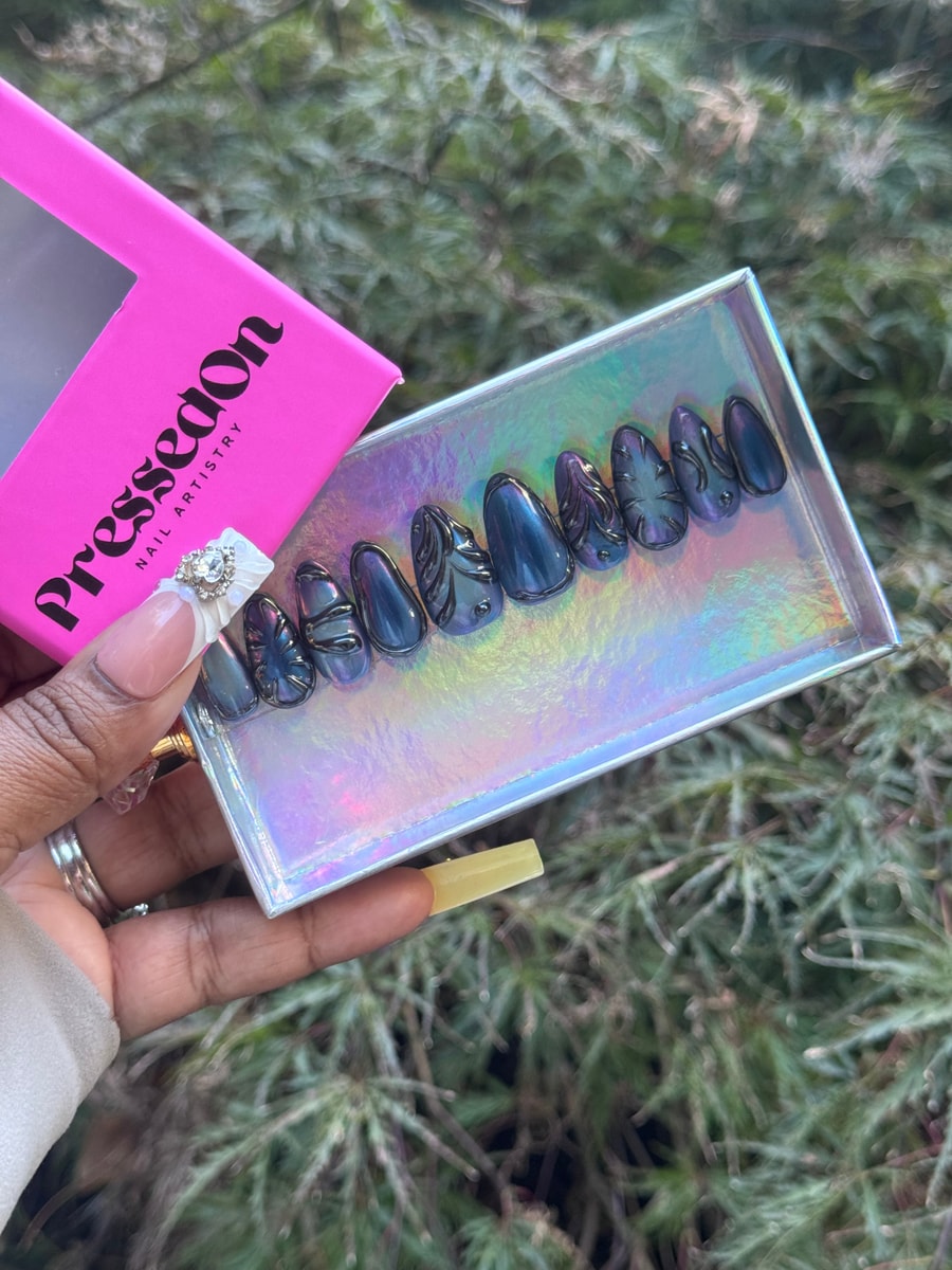 Short press-on nails with a dark midnight marble finish and sculpted elements on the surface.