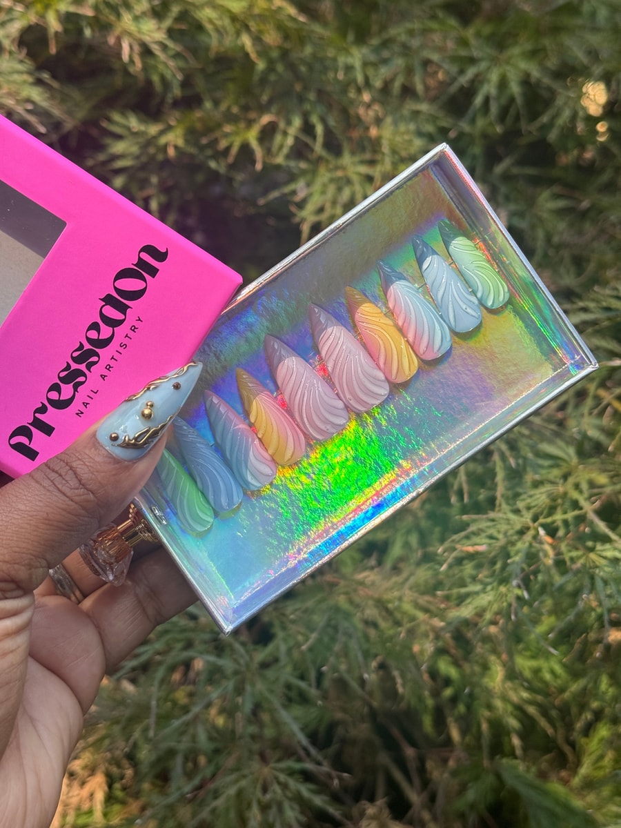 These are short stiletto press-on nails with a 3D swirl design. The set features pastel colors including blue, pink, yellow, green, and gray.