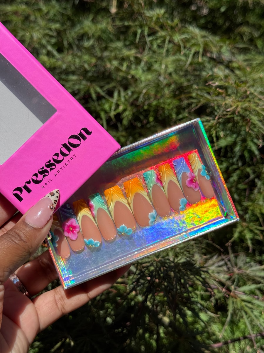 Almond-shaped press-on nails with a multi-colored French tip design and 3D flower embellishments in shades of blue, pink, green and orange.