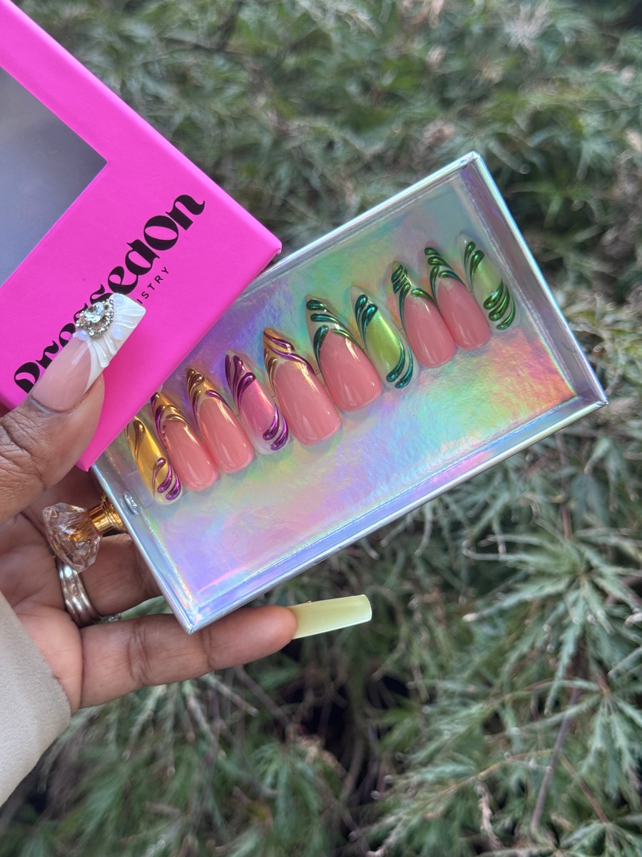 Medium length press-on nails featuring a pink base with metallic gold, purple and green French tips, and subtle 3D swirl designs.