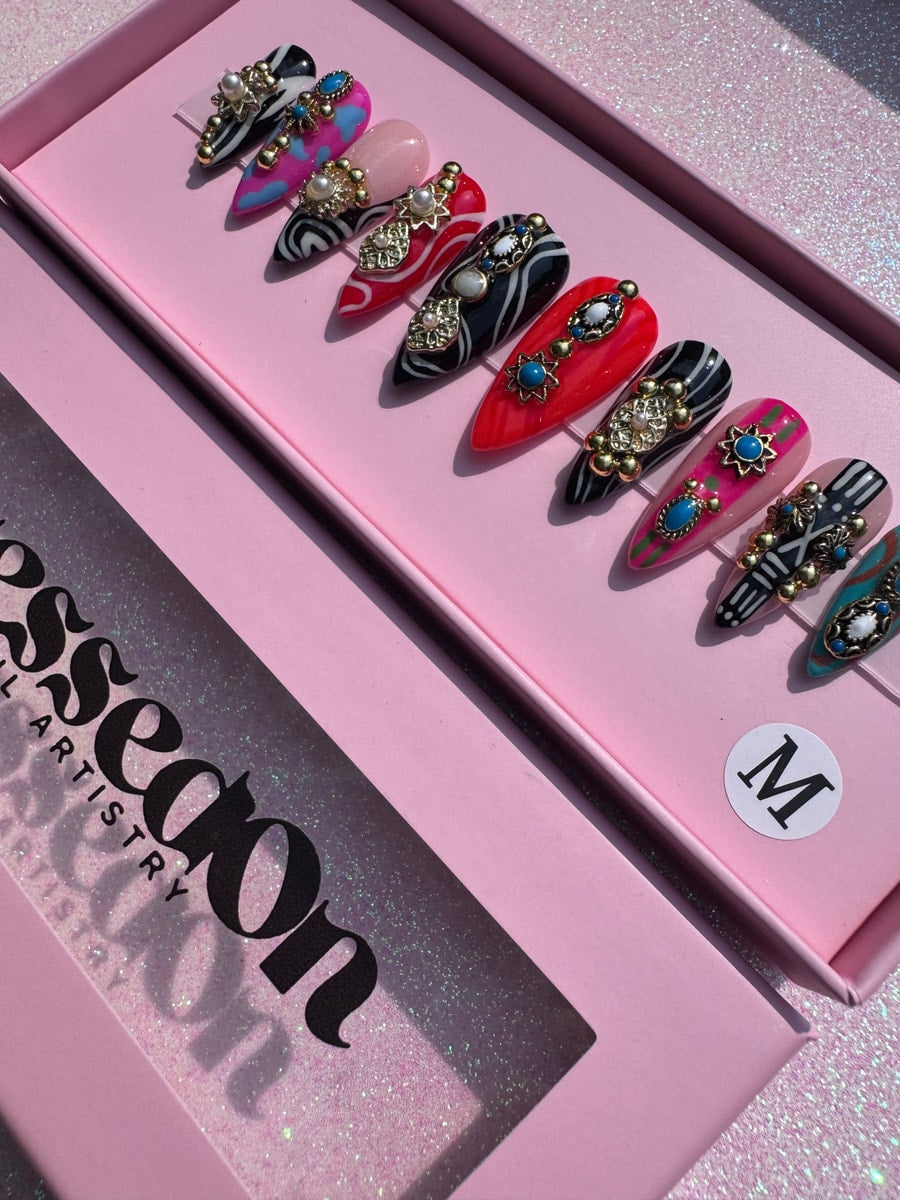 A set of junk style press-on nails with a variety of designs including zebra stripes, pink, red, and turquoise, all adorned with gold beads and pearl accents.